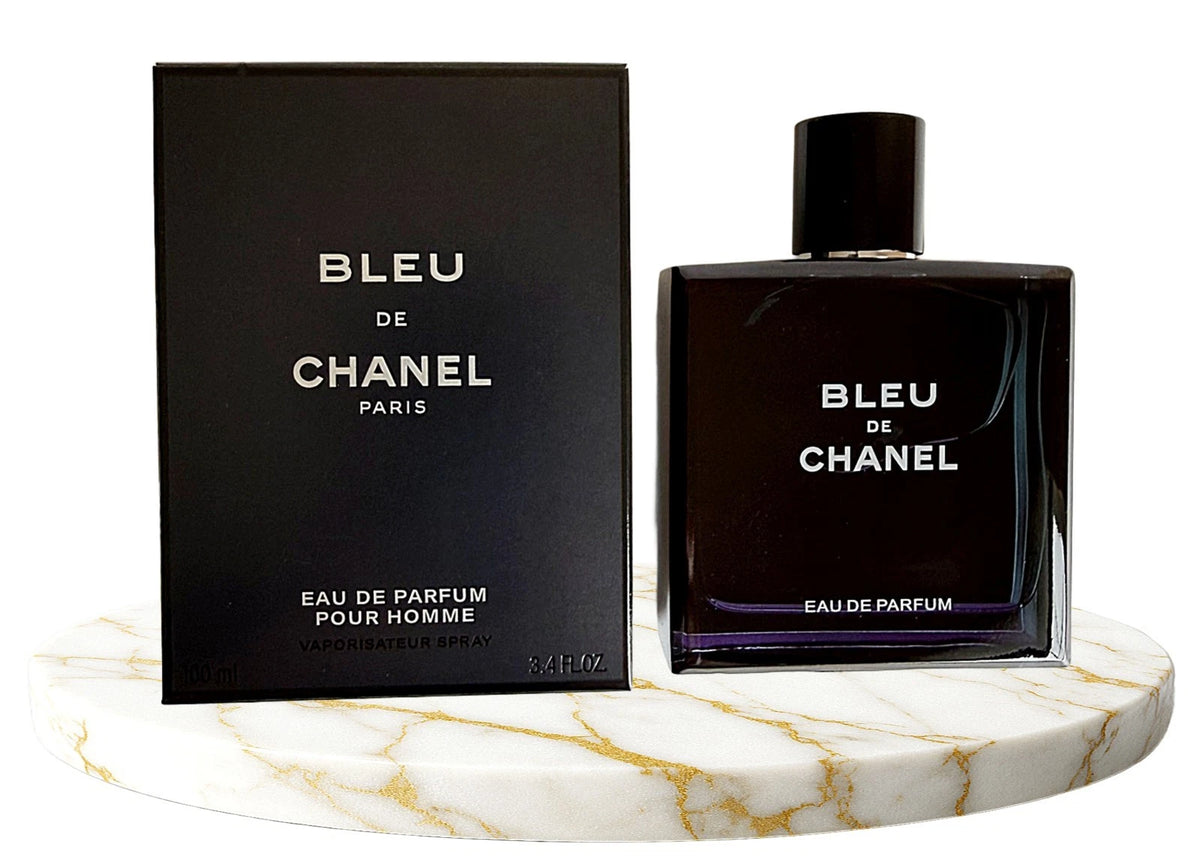 Chanel Bleu de Chanel Eau de Parfum bottle and its black packaging box, displayed on a white marble round tray with gold veining against a white background.